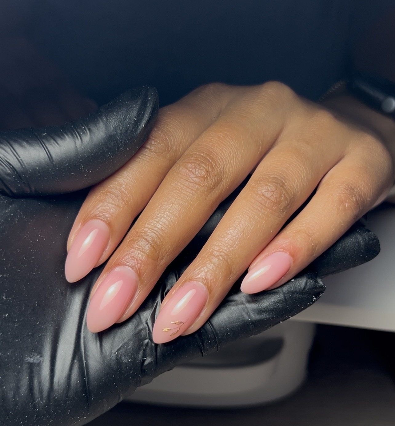 Nude-roze amandelnagels, vastgehouden met een zwarte handschoen